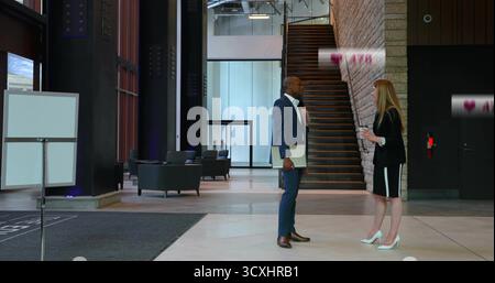 Stehende Kollegen in Anzügen, die eine Kaffeetasse und einen Laptop in der Lobby mit Schild halten Stockfoto