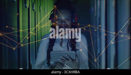 IT-Techniker analysiert Netzwerkdiagramme im LED-beleuchteten Server-Rack-Gang mit Tablet und roten Kopfhörern Stockfoto