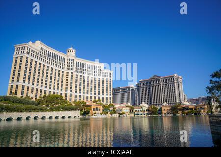 Die Hotels Bellagio und Caesars Palace spiegeln sich im Bellagio-See wider, umgeben von Grün und hellblauem Himmel an einem warmen Nachmittag in Nevada Stockfoto