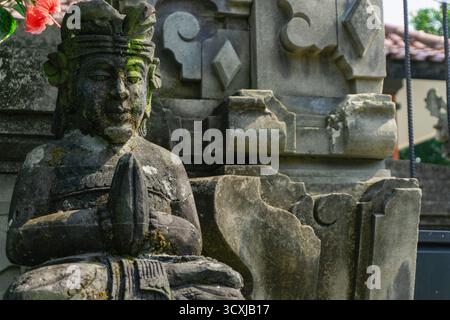 Diese Nahaufnahme des Kopfes und des Oberkörpers einer balinesischen Hindugottsstatue, bedeckt mit dickem Moos, vermittelt ein Gefühl von Alter und tiefem Kulturerbe Stockfoto