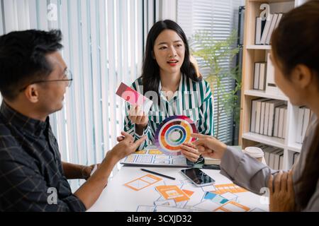 Eine Gruppe von UX/UI-Designern arbeitet gemeinsam kreative Ideen aus und diskutiert Farbpaletten und Layoutkonzepte für eine neue mobile Anwendungsoberfläche Stockfoto