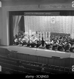 Ein Archivfoto aus dem Jahr 1984 zeigt ein Sinfonieorchester auf der Bühne des Artem Palastes der Kultur in Sloviansk, Ukrainische SSR. Ein Dirigent führt die Musiker vor einem Publikum, das im Saal sitzt. Über der Bühne zeigt ein prominentes Banner den klassischen leninistischen Slogan: „Kunst gehört dem Volk“. Die Szene fängt das reiche kulturelle Leben einer typischen sowjetischen Industriestadt ein. Dieses Bild ist ein wertvolles Dokument der Kunst und Ereignisse der Gemeinschaft in einem friedlichen Donbass vor dem Krieg Stockfoto