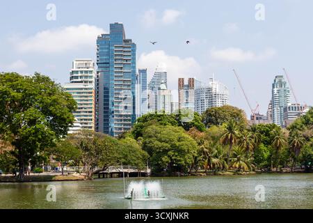 Lumphini Park in Bangkok, Thailand, mit einem Teich mit Brunnen und Blick auf die moderne Skyline der Stadt. Stockfoto