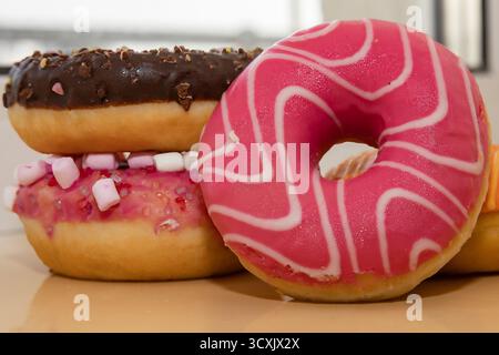 Bunte Donuts mit rosafarbener Schokolade und Marshmallow-Glasur auf beigem Hintergrund Stockfoto