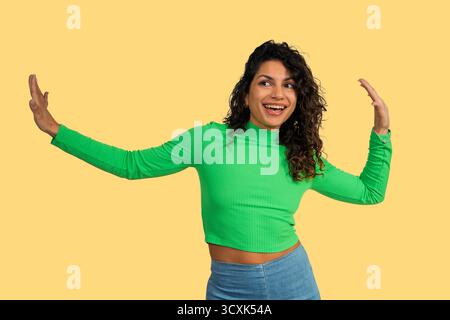 Junge Frau tanzt mit einem großen Lächeln und ausgestreckten Armen, die Freude und Aufregung ausdrücken Stockfoto