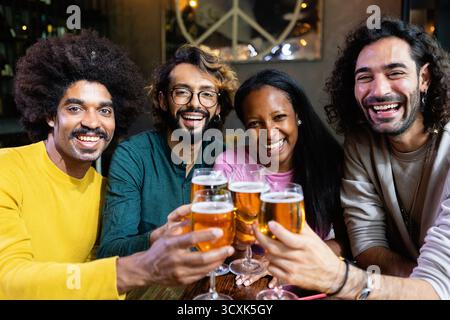 Fröhliche, multiethnische Freunde, die mit Biergläsern an der Bar getoast haben Stockfoto