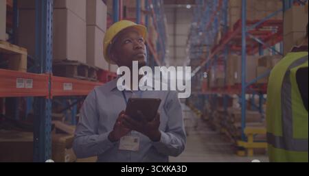 Mitarbeiter, die den Lagerbestand mit Tablettenbeständen in Lagergängen überprüfen und Sicherheitsausrüstung zwischen Regalen und Kisten tragen Stockfoto