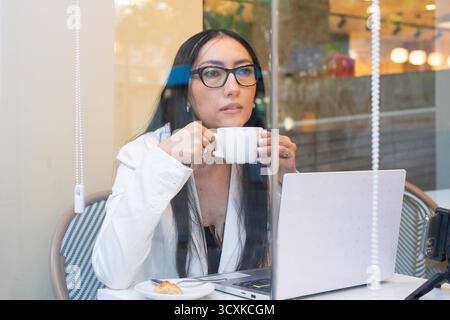 Frau mit Brille, die sich während der Fernarbeit oder beim Lernen in einem Café fokussiert Stockfoto