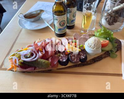 Schwarzwald, Deutschland - 27. Dezember 2023: Traditionelle deutsche Vesper-Platte in einem Schwarzwaldrestaurant mit verschiedenen Aufschnitten, Würstchen, Blutwurst, Pastete, Gurken, Zwiebeln, Ei, Käseaufstrich und lokale Bierflaschen Stockfoto