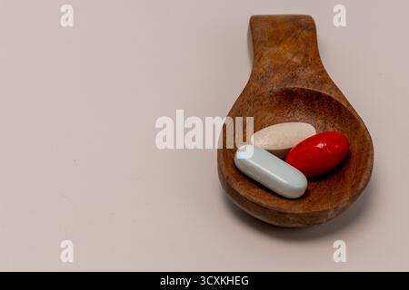 Weiche rote und gelbe Gelatinekapseln mit blauer und weißer Tablette in einem Holzlöffel Stockfoto