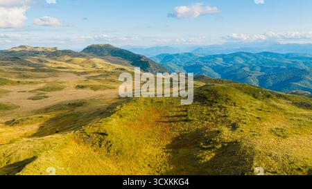 Friedlicher Blick aus der Luft auf Bergwiesen und sanfte Hügel, beleuchtet vom Sommertageslicht Stockfoto
