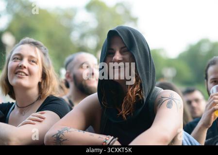 Sofia, Bulgarien — 25. Juni 2025. Eine lächelnde Frau in schwarzer Kapuze und Tattoos genießt die Live-Rock-Konzertatmosphäre, die Individualität und Konkretheit widerspiegelt Stockfoto