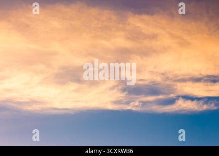 Orangefarbene Wolke am blauen Himmel bei Sonnenuntergang. Wunderschöner Naturhintergrund in der Abenddämmerung für Meteorologie. wolkenlandschaft in gelbem Licht. Abstrakte Szene des Sommerwetters Stockfoto