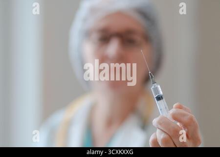 Nahaufnahme eines Arztes in einer weißen Uniform mit einer Spritze. Der Schwerpunkt liegt auf der Spritze, die mit dem Medikament gefüllt ist. Symbol für Gesundheit, Prävention und medizinische Verantwortung. Stockfoto