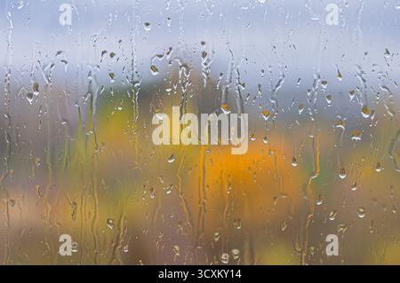 Abstrakte Wasserstreifen und -Tropfen laufen durch das Fenster und verwischen die orange Herbstlandschaft. Fließende Feuchtigkeit sorgt für saisonale Textur, natürlichen Hintergrund, Stockfoto