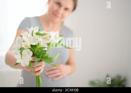Heitere Nahaufnahme der Hände der Schwangeren mit weißen Blüten sanft auf rundem Bauch. Herzerwärmende pränatale Bindungsszene. Stockfoto
