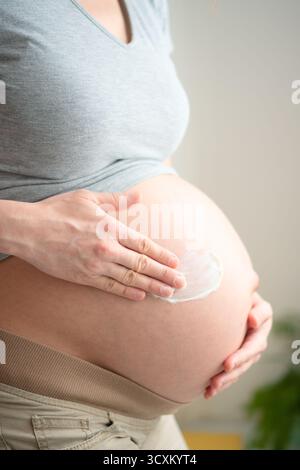 Nahaufnahme einer zukünftigen Mutter, die pflegende Creme auf ihren wachsenden Bauch aufträgt. Wichtiges Hautpflegeritual zur Erhaltung der Hautelastizität während der Schwangerschaft. Stockfoto