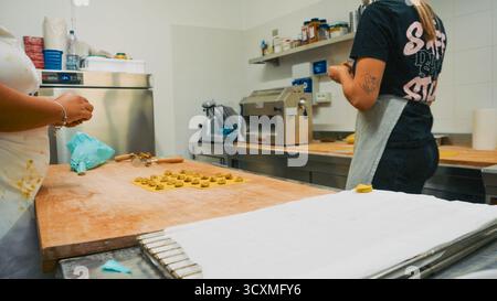 Piacenza, Italien - 1. Oktober 2025 zwei Frauen arbeiten zusammen in einer professionellen Küche und bereiten kleine Nudelformen auf einem Holztisch mit Kocheinrichtung vor Stockfoto
