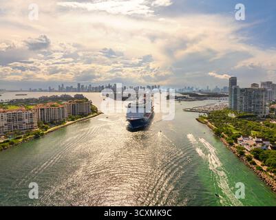Großes Passagier-Kreuzfahrtschiff, das am Hauptkanal im Hafen von Miami in der Nähe von South Beach hochluxuriöse Hotels und Apartmentgebäude ablegt. Stockfoto