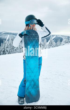 Porträt einer Frau, die ein Snowboard hält und Skibrille trägt Stockfoto