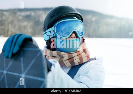 Porträt einer Frau, die ein Snowboard hält und Skibrille trägt Stockfoto