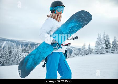 Porträt Der Frau Auf Dem Hintergrund Der Berge. Ein Snowboard halten und Skibrille tragen. Stockfoto