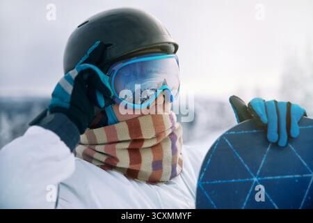 Porträt Der Frau Auf Dem Hintergrund Der Berge. Ein Snowboard halten und Skibrille tragen. Stockfoto