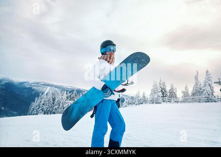 Porträt Der Frau Auf Dem Hintergrund Der Berge. Ein Snowboard halten und Skibrille tragen. Stockfoto