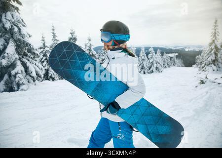 Porträt einer Frau, die ein Snowboard hält und Skibrille trägt. Skibrille Von Snowboardern Mit Dem Spiegelbild Der Verschneiten Berge. Wintersport. Stockfoto