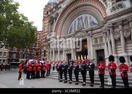 Tri-Service-Mitarbeiter der Royal Navy, der Royal Air Force und der Army säumen den Weg zur Kathedrale, während die Trägerpartei, bestehend aus Mitgliedern der Walisischen Garde, den Sarg, der mit einer Flagge von Union Jack versehen ist, zur Requiem-Messe für den ehemaligen Chef der Streitkräfte, Feldmarschall Lord Guthrie, in der Westminster Cathedral im Zentrum Londons trägt. Bilddatum: Mittwoch, 15. Oktober 2025. Stockfoto