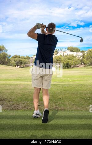 Rückansicht eines jungen Mannes, der an einem sonnigen Tag mit blauem Himmel auf dem Golfplatz Golf spielt. Stockfoto