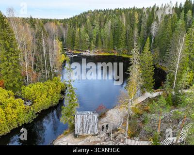 Aus der Vogelperspektive auf einen dunklen, ruhigen Pool in einem Fluss, der von einem herbstfarbenen nördlichen Wald und hölzernen Besucherstegen und Plattformen umgeben ist Stockfoto