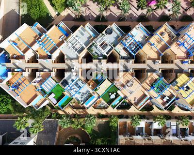Blick von oben auf farbenfrohe Dachterrassen, Sonnenliegen, Pergolen und private Bereiche in einem Wohnkomplex im mediterranen Stil mit Palmen Stockfoto