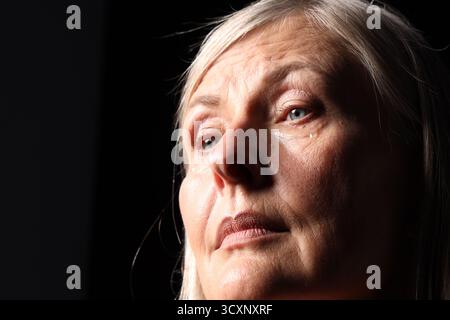 Ältere Frau weint auf schwarzem Hintergrund, Nahaufnahme. Leerzeichen für Text Stockfoto