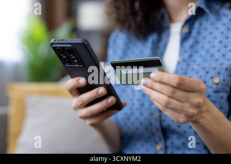 Frau, die ein schwarzes Smartphone und eine grüne Kreditkarte hält, während sie sicher von zu Hause aus online kauft, konzentriert sich auf mobile Zahlungen, App und private CA Stockfoto