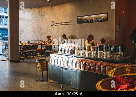Starbucks Coffee Shop innen, Leute sitzen an den Tischen und eine Auswahl an Kaffeebohnenpaketen im Vordergrund Stockfoto