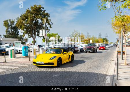 Olhao, Portugal, 12. Oktober 2025. Ein gelber Porsche Boxster fährt an anderen Fahrzeugen und Fußgängern in der belebten Innenstadt vorbei. Stockfoto