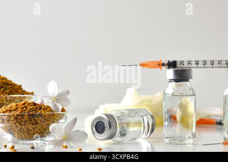Pollenimpfkonzept mit Durchstechflaschen mit Impfdosen und Spritze oben, reflektiert auf einem weißen Tisch mit einer Schüssel voller Allergene. Vorderansicht. Stockfoto