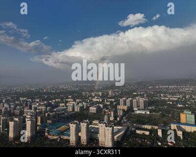 Überblick über die Stadt mit städtischen Gebäuden und grünen Hügeln unter einem dramatischen Himmel mit einer großen Sturmwolke und einem hellen Regenbogen, der sich über der Dista erhebt Stockfoto