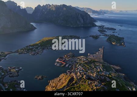 Das Fischerdorf reine und der Hafen liegen zwischen dramatischen Berggipfeln und tiefblauen Fjorden, in denen traditionelle rote rorbuer-Hütten auf der Küste zu sehen sind Stockfoto