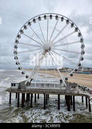 Der Pier Skyview: riesenrad in der Nordsee auf dem Pier in Scheveningen, Niederlande mit dunklen Wolken bei Herbstwetter; Strand im Hintergrund Stockfoto