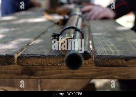 Antikes Feuerstein-Gewehr auf einem rustikalen Holztisch mit verschwommenen Händen im Hintergrund, historische Waffen aus Nahaufnahme zur Nachstellung oder Museumsdiskretion Stockfoto