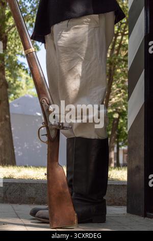 Ein Reenactor in historischer Tracht, der mit einer alten Feuersteinmuskete in der Nähe eines Gebäudes steht Stockfoto