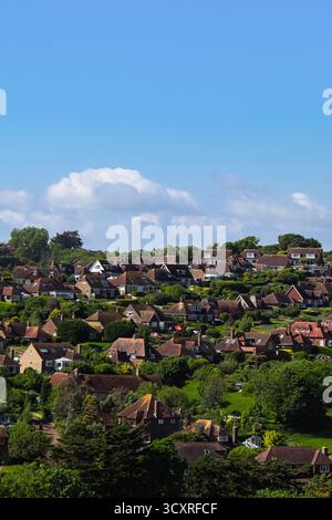 Wohnhäuser und Dächer auf einem grünen Hügel mit blauem Himmel und weißen Wolken. East Sussex Country, England Stockfoto