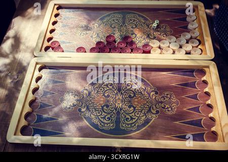 Ein wunderschönes offenes Backgammon-Brett aus Holz mit roten und weißen Karomustern für ein Spiel im Sonnenlicht im Freien Stockfoto