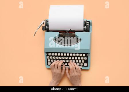 Frau tippt auf Schreibmaschine mit leerem Papierbogen auf beigem Hintergrund Stockfoto