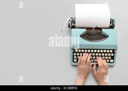 Frau, die auf einer Schreibmaschine mit leerem Papierbogen auf grauem Hintergrund schreibt Stockfoto