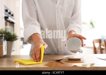Frau, die mit einem Lappen verschütteten Kaffee auf dem Tisch in der Küche abwischt, Nahaufnahme Stockfoto