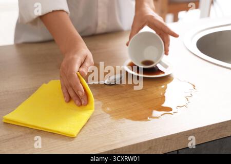 Frau, die mit einem Lappen verschütteten Kaffee auf dem Tisch in der Küche abwischt, Nahaufnahme Stockfoto