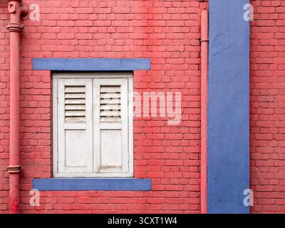 Weißes Holzfenster geschlossen mit roten Ziegelwänden, Rohren und einigen blau lackierten Bereichen. Stockfoto